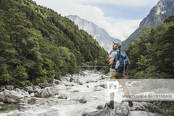 Reifer Mann mit Rucksack steht auf einem Felsen am Fluss