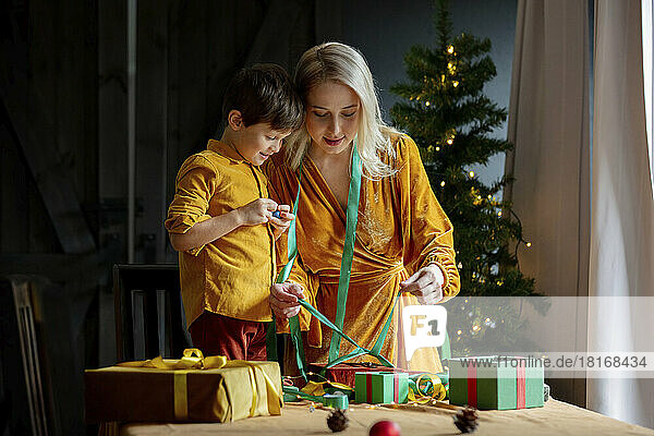 Frau zeigt Sohn  wie man eine Schleife an ein Geschenk bindet