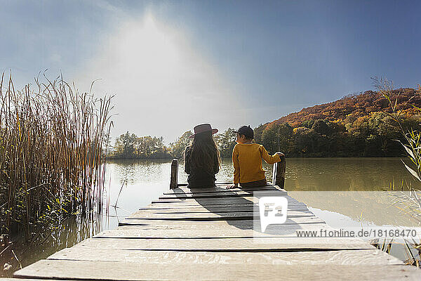 Boy and girl sitting on jetty on sunny day