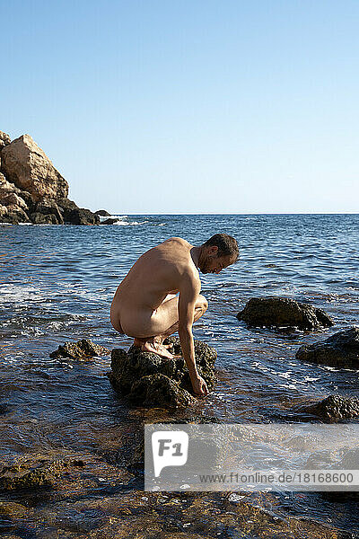 Nackter Mann sitzt an einem sonnigen Tag auf einem Felsen inmitten des Meeres
