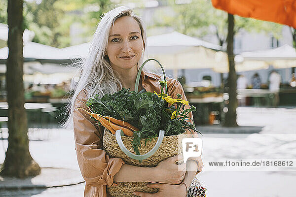 Customer holding organic vegetable and flowers in wicker bag at market