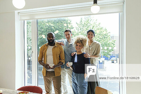 Smiling business people standing in front of window holding cups of coffee