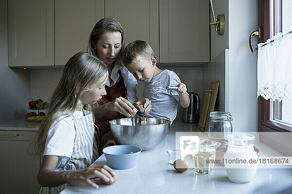 Mother and children preparing cake in kitchen at home
