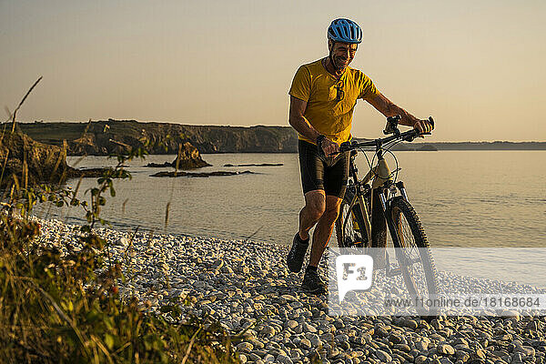 Happy mature man walking with bicycle at beach