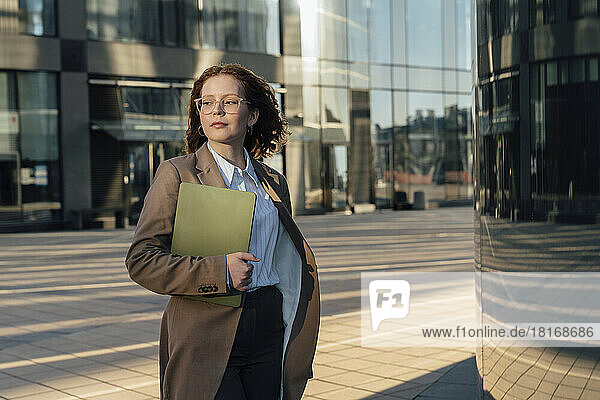Young businesswoman with laptop by office building in city
