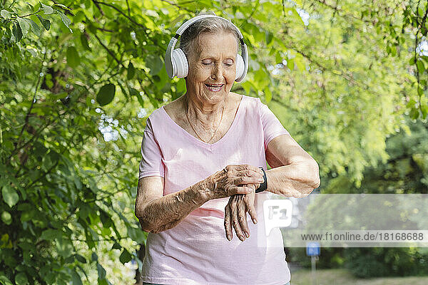 Smiling senior woman with smart watch listening to music through headphones in park