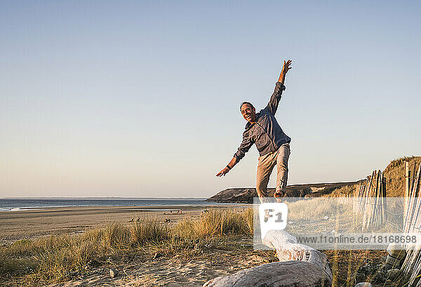 Cheerful mature man having fun on log at beach