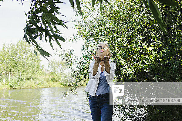 Senior woman blowing kiss standing near plants