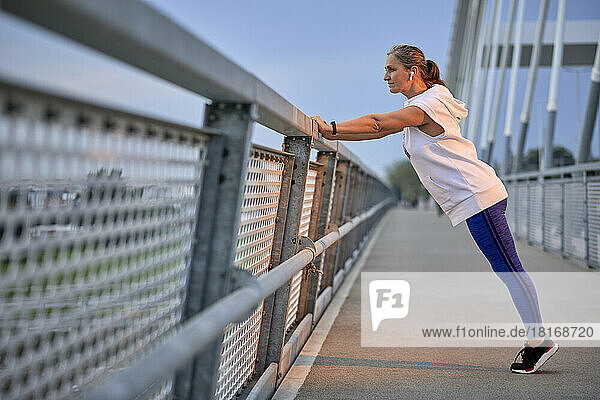 Woman exercising near railing on bridge