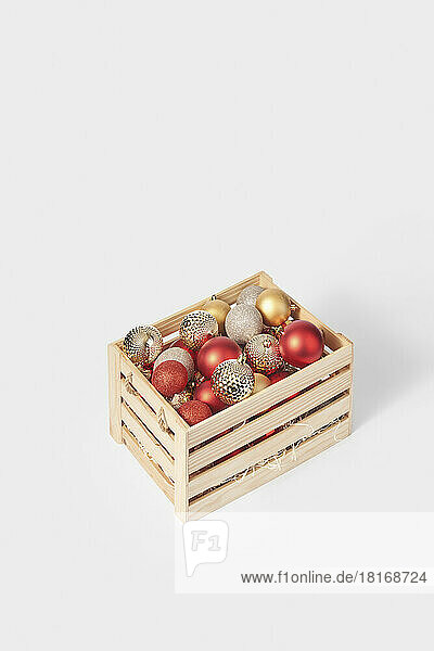 Shiny christmas baubles in wooden box against white background