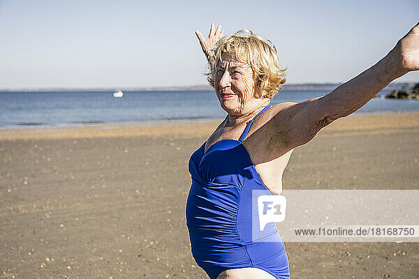 Smiling senior woman with arms outstretched standing at beach