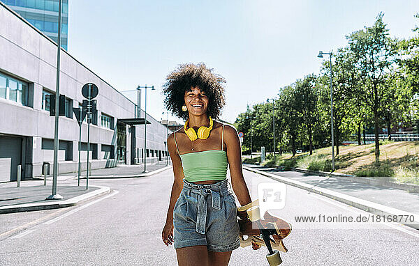 Glückliche junge Frau mit Skateboard  die auf der Straße läuft