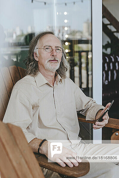 Contemplative senior man with tablet PC sitting on chair