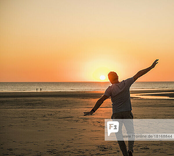 Mann mit ausgestreckten Armen amüsiert sich am Strand bei Sonnenuntergang