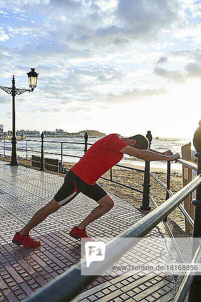 Man exercising by railing on promenade