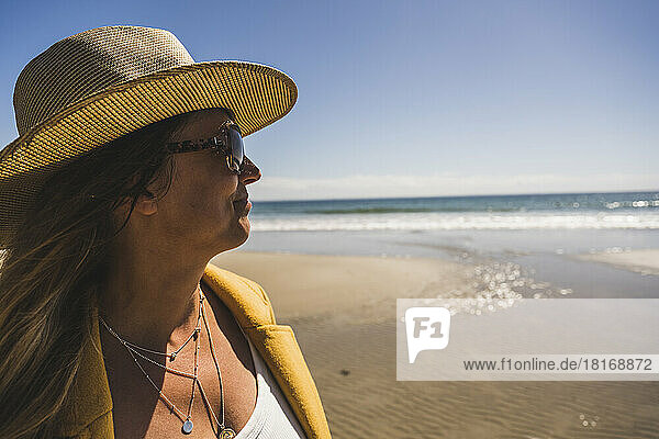 Reife Frau mit Hut und Sonnenbrille am Strand an einem sonnigen Tag