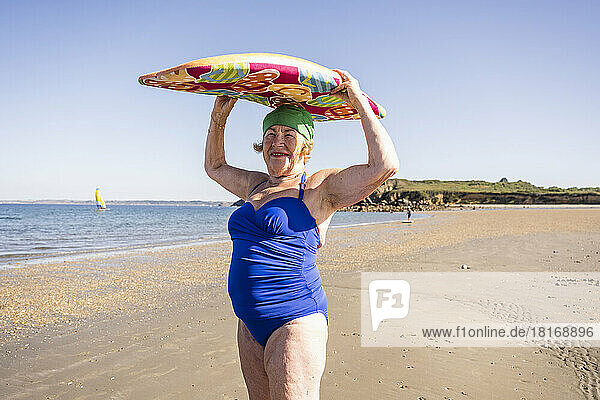 Senior woman carrying surfboard on head at beach