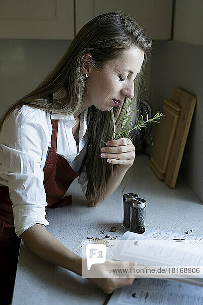 Woman with eyes closed smelling rosemary in kitchen at home