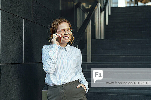 Lächelnde Geschäftsfrau  die im Treppenhaus mit dem Mobiltelefon telefoniert