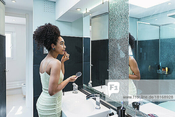 Woman with curly hair applying make-up on face in bathroom at home