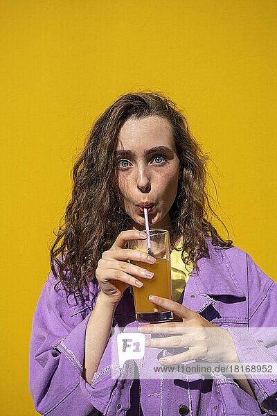 Frau mit braunen Haaren trinkt Saft vor gelber Wand