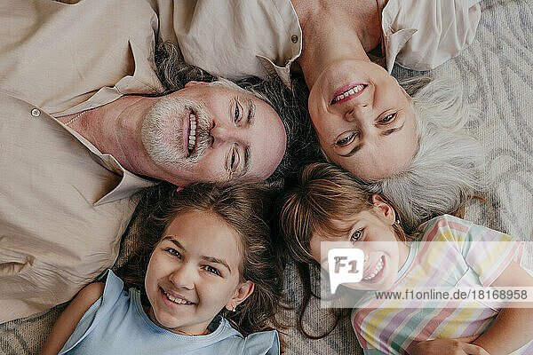 Happy grandparents and granddaughters lying together with heads in circle at home