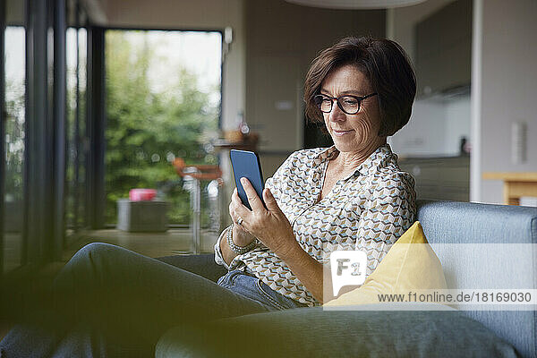 Lächelnde ältere Frau  die zu Hause ihr Smartphone benutzt