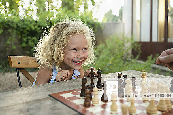 Cheerful blond girl with chessboard on table in garden