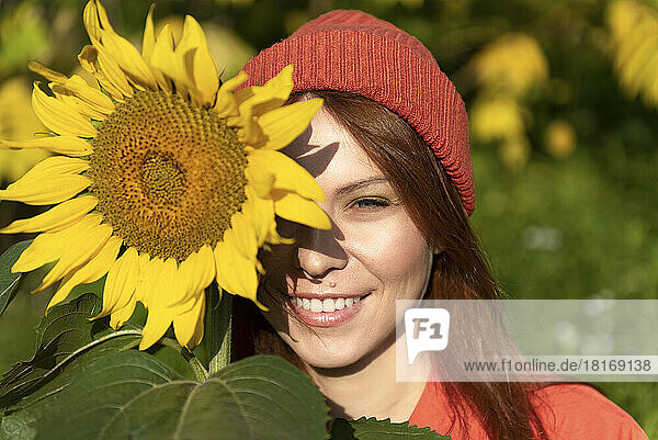 Lächelnde Frau mit Strickmütze und Sonnenblume an einem sonnigen Tag