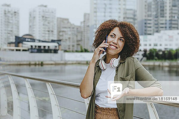 Smiling young woman talking through smart phone leaning on railing