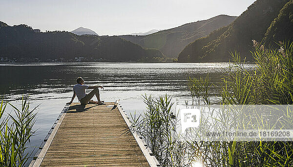 Mature man with laptop looking at lake and mountains from jetty