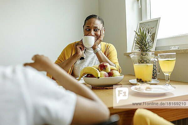 Smiling woman drinking coffee at dining table