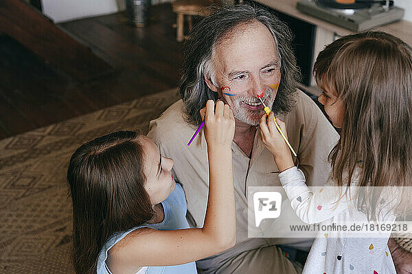 Playful children having fun painting grandfather's nose at home