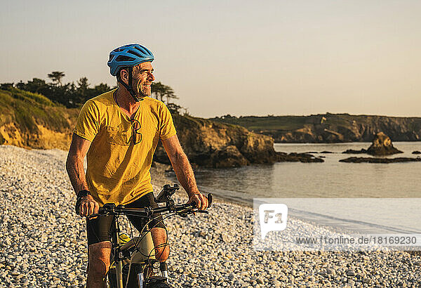 Smiling mature man riding bicycle on shore at sunset