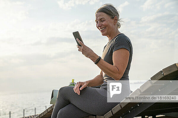 Happy woman looking at mobile phone on wooden bench