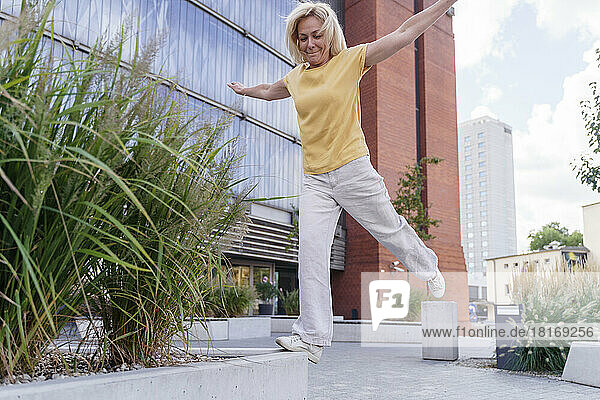 Happy woman with arms outstretched balancing on planter
