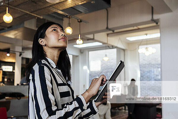 Young businesswoman standing in coworking office using digital tablet