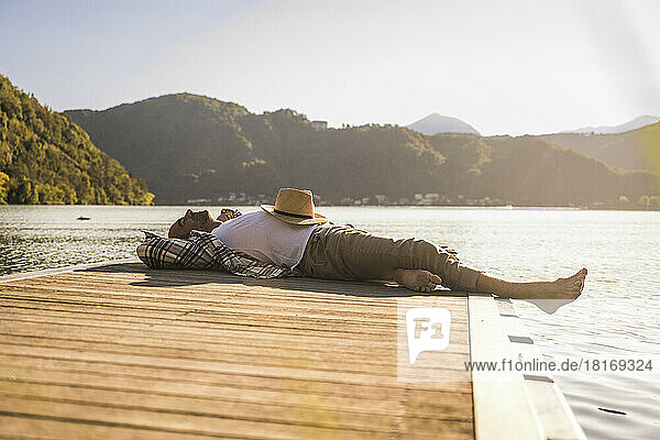 Man with hat resting on jetty over lake
