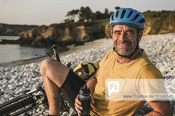 Happy man with cycling helmet relaxing on shore at beach