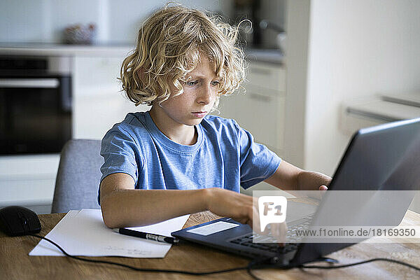 Junge mit blonden Haaren benutzt Laptop auf Tisch zu Hause
