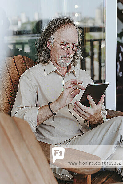 Senior man sitting on chair and using tablet PC at home terrace