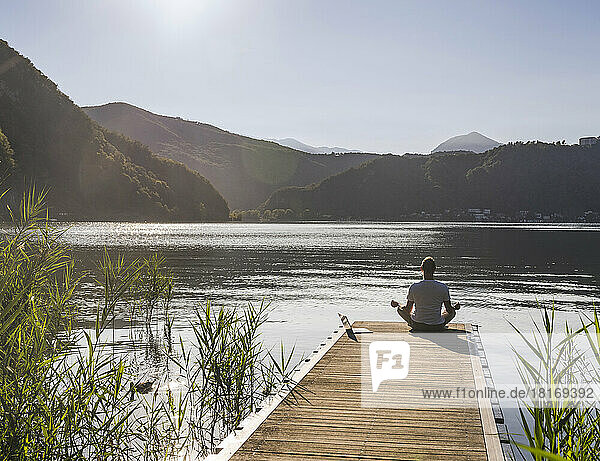Man with laptop meditating on jetty over lake