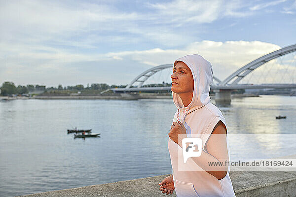 Woman wearing hooded shirt jogging by river