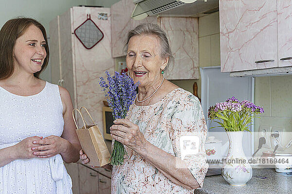 Smiling senior woman looking at lavender flowers by granddaughter in kitchen