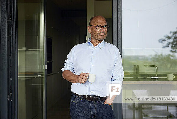 Smiling man with coffee cup leaning on glass door