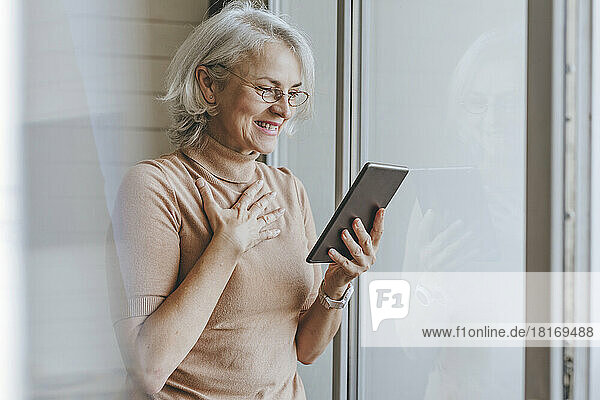 Glückliche reife Frau bei Videoanruf über Tablet-PC zu Hause