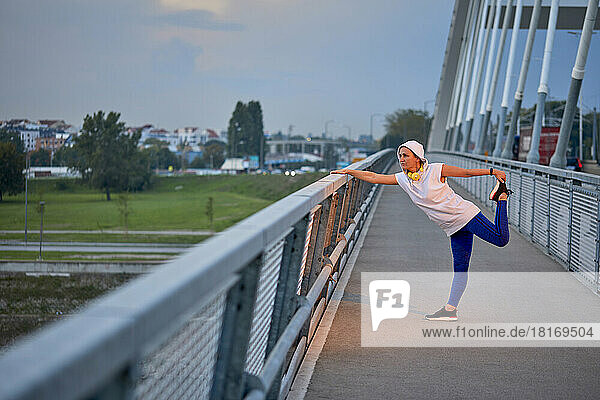 Mature woman stretching legs standing on bridge