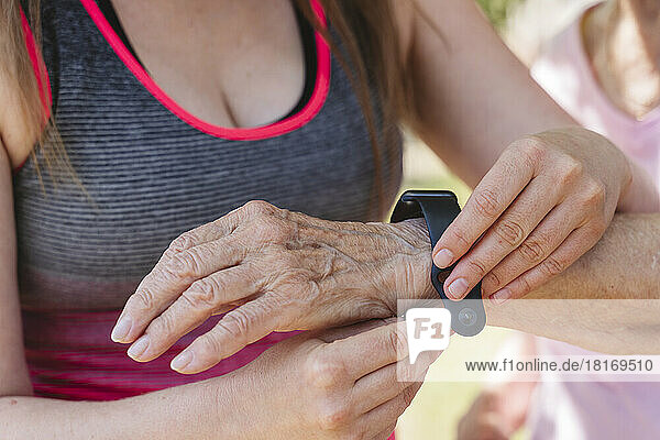 Fitnesstrainer justiert Smartwatch an der Hand einer älteren Frau