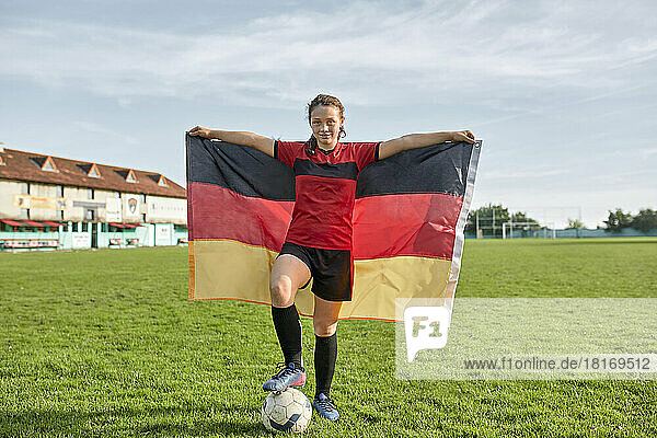 Girl standing with German flag on field under cloudy sky