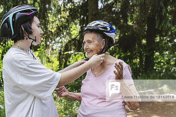 Girl helping great grandmother wearing bicycle helmet in park